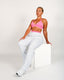 Woman wearing a pink sports bra and grey sweatpants sitting on a white block against a light gray background