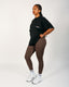 Person wearing a black oversized t-shirt, brown leggings, and white sneakers on a white background