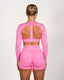 Person wearing a pink athletic outfit with long sleeves and open back on a white background