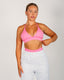 Woman wearing a pink sports bra and light gray sweatpants on a plain background