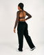 Person wearing a brown long-sleeve top with sheer back and black cargo pants on a white background